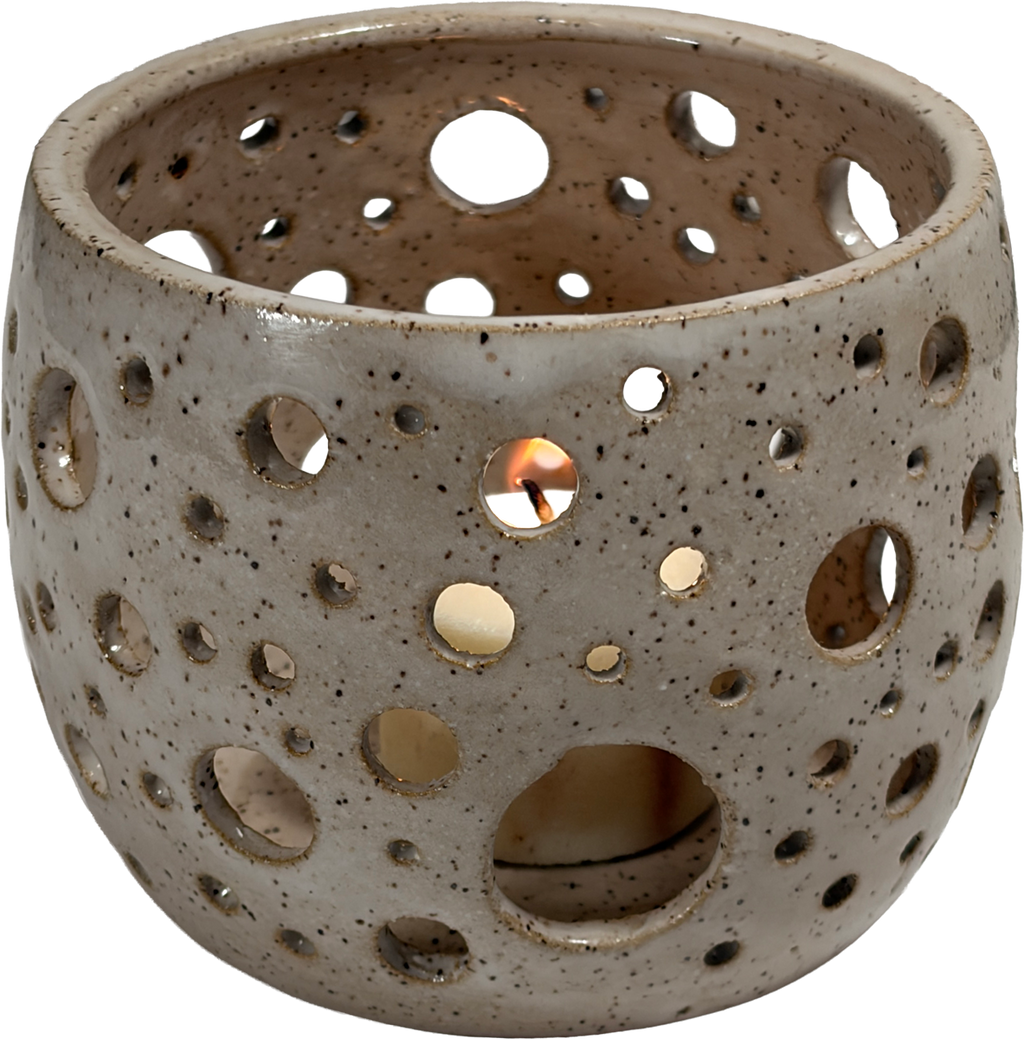A ceramic candle holder with a speckled beige and gray glaze, featuring multiple circular cutouts that reveal a lit candle inside, set against a plain white background.