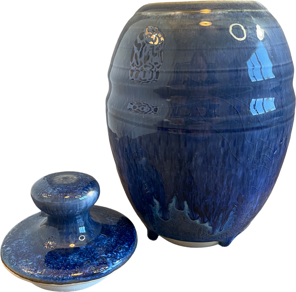 A glossy cobalt blue ceramic jar with a matching lid, displayed on a clean white background. The jar features a textured, crackled glaze with lighter blue and white veining, and the lid has a matching rounded knob.