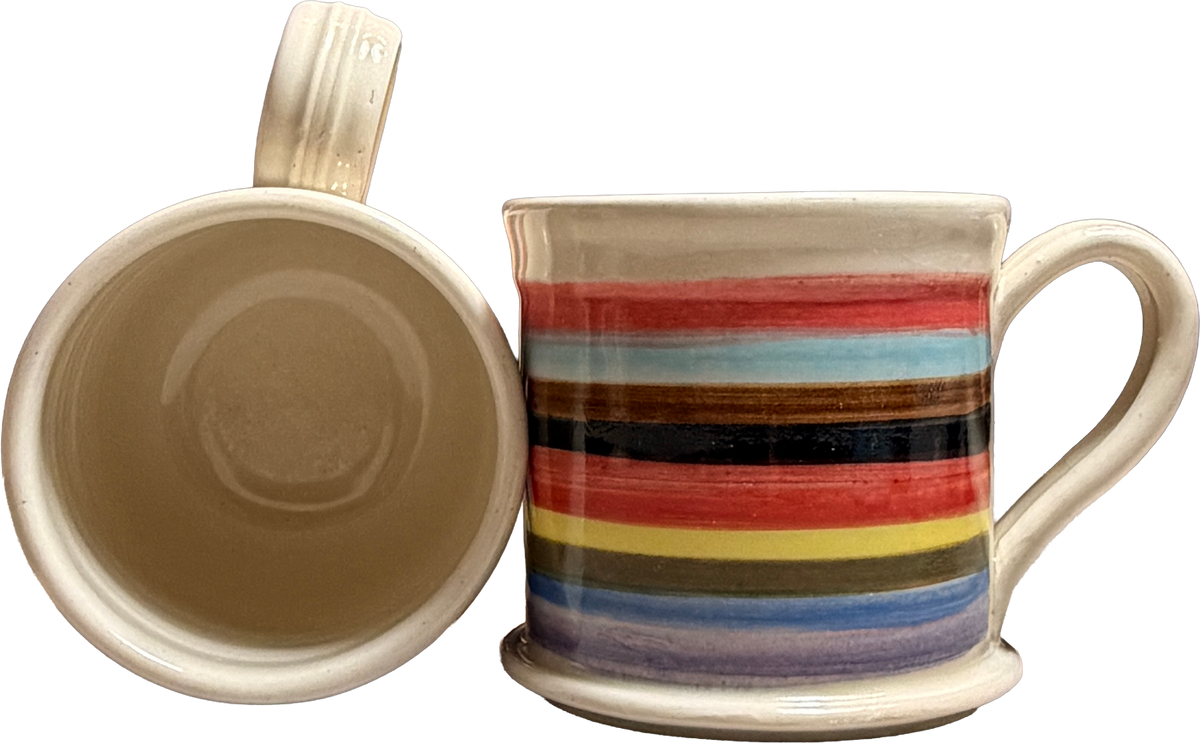 A ceramic mug shown from two angles: one view shows the interior with a beige glazed finish, and the other shows the exterior decorated with horizontal stripes in red, light blue, brown, black, yellow, and purple on a cream base.
