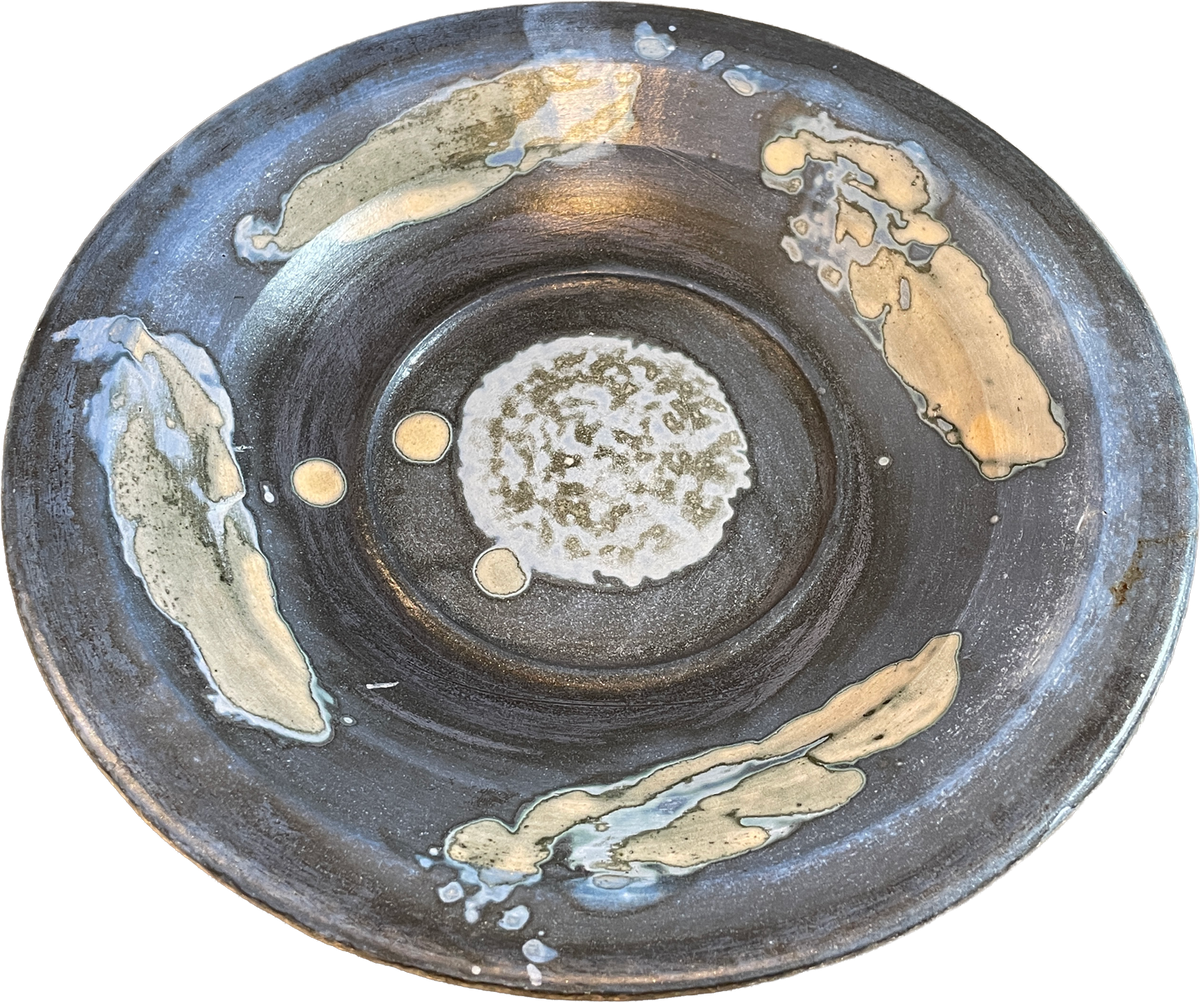 A round handmade ceramic plate with a dark charcoal gray glaze, featuring abstract hand-painted gold and beige brushstrokes and a textured white and green center.